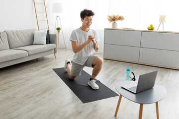 Cheerful Asian guy doing forward lunges in front of laptop