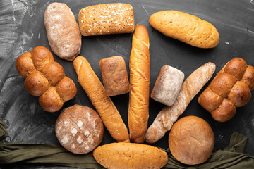 a lot of fresh bread on a black background, top view. Homemade fresh pastries of various loaves of wheat and rye bread close-up.