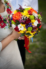 Wedding multi-colored bright bouquet in the hands of the bride in the hands on the street in a wedding dress with Ukrainian embroidery
