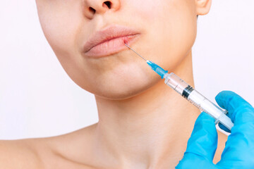 Cropped shot of young woman's face with syringe needle on her lips held by doctor's hand in a blue...