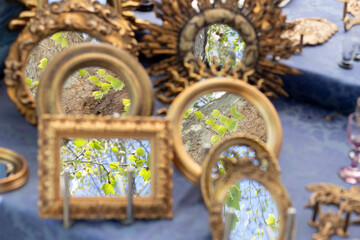 Antiques market, detail with a series of small frames in gilded wood. Selective focus on the foliage of a tree reflected in the mirrors.