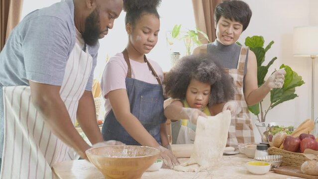 African American family with daughter rolling for thresh flour for cooking with father and mother together in the kitchen at home, parent and little child activity preparing food with fun.