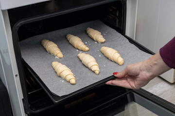 a woman puts croissants lying on a baking sheet into the oven