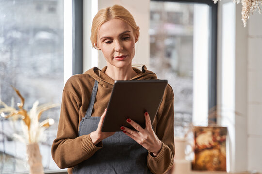 Woman smiling while looking at the tablet screen while spending time at her workplace