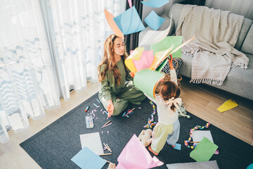 Mother doing yoga exercise, meditating while little daughter playing, throwing paper. - obrazy, fototapety, plakaty