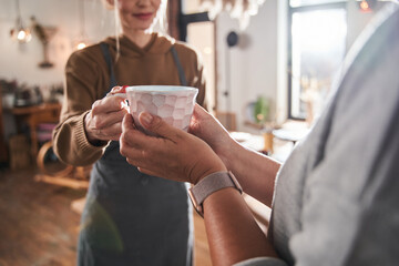 Female artist giving cup of hot tea to her senior student at the art studio at her master class