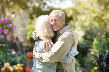 Loving elderly couple hugging each other during walk in their own garden in countyside, enjoying their vacation