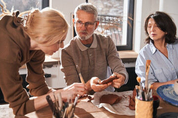 Grey haired bearded man asking his teacher while spending time at the pottery workshop