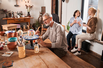 Senior man drawing at the hand made ceramic teapot during the pottery master class