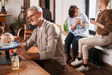 Senior man sitting at the table and drawing his own patterns at the hand made teapot