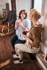 Obraz premium Women holding cups of hot beverage and talking with each other after ceramics master class