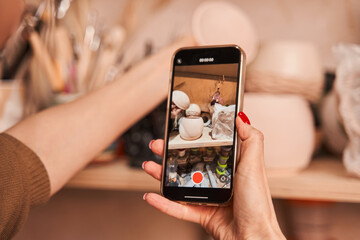 Woman artist shooting ceramic vase and cups at the smartphone