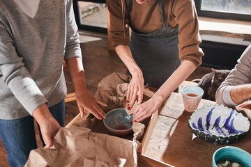 Two women putting new hand made plate at the paper and cupboard box while packing