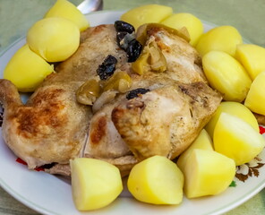 Fried chicken with prunes and boiled potatoes on a plate close-up