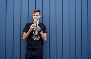 Young street musician playing the trumpet near the big blue wall