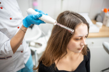 Obraz na płótnie Canvas Professional beautician doing darsonval hair treatment procedure for young woman in beauty salon