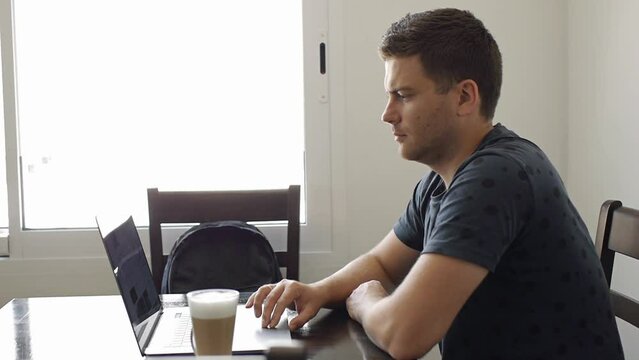 Freelancer businessman scrolling touchpad of silver laptop at coffeeshop. A clear glass of coffee with milk on the table. Medium shot