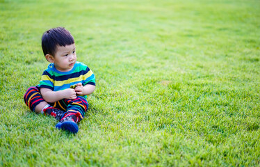 Kid sit thoughtful on the grass with idea space. Cute baby boy in a striped colorful t shirt sit and play in the garden on a Sunny summer day. Little child sit and playing dry leaves in the park.