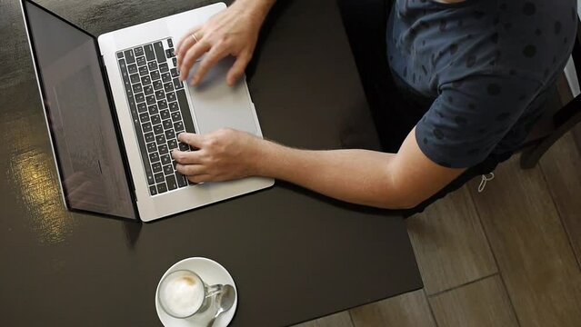 Freelancer businessman scrolling touchpad of silver laptop at coffeeshop. A clear glass of coffee with milk on the table. High angle view