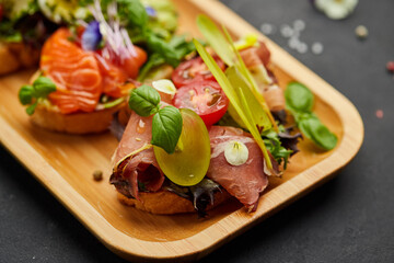 Assorted bruschetta set with salmon, parma and pesto souce. Italian antipasti snacks. Variety mix of small sandwiches on dark background. Photo for restaurant menu