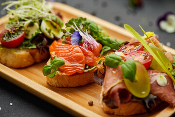 Assorted bruschetta set with salmon, parma and pesto souce. Italian antipasti snacks. Variety mix of small sandwiches on dark background. Photo for restaurant menu