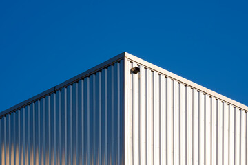 Sunlight reflection on surface of corrugated steel wall of warehouse building against blue clear...