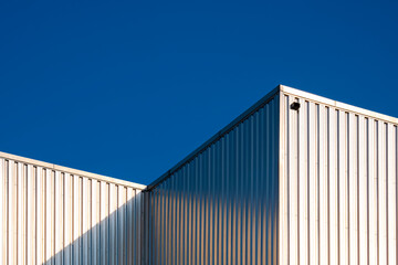 Fototapeta na wymiar Sunlight reflection on surface of corrugated steel wall of industrial building against blue clear sky background in low angle view