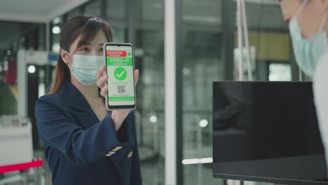 Asian Businesswoman wearing face mask showing vaccine information on smartphone at check in counter in airport, travel under Covid-19, New normal, Illness Prevention, Immunization Certificate concept