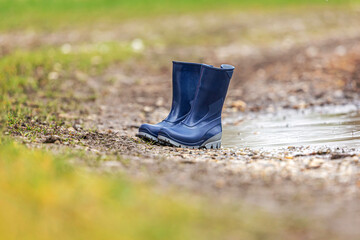 Focus on blue rubber boots near a puddle at a rainy day