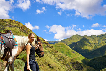 Fototapeta premium On top of the world. A young woman with her horse on a mountain trek.