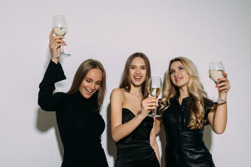 Young happy women friends posing isolated over white wall background drinking champagne on a party.