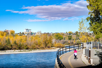 A person jogging on a bike path along the Bow River at an outdoor park in downtown Calgary Alberta Canada.
