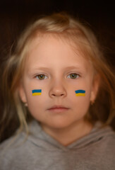 Sad Ukrainian child girl with a painted flag on his cheeks. Pray for Ukraine.