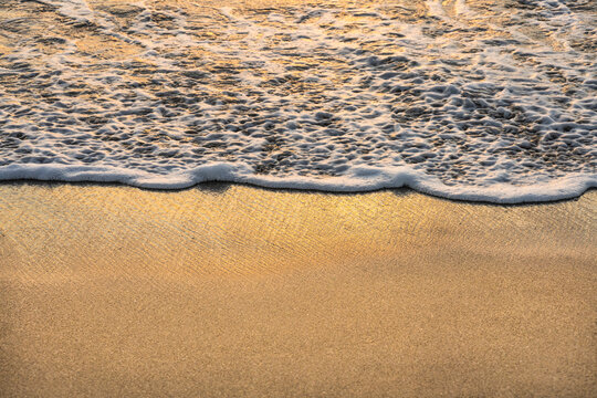 Close-up&nbsp;of ocean wave on sand at sunset