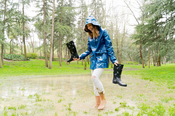 front view of woman walking barefoot on pond holding galoshes. Horizontal panoramic view of woman splashing with mud on rainy pond. Nature and people backgrounds.