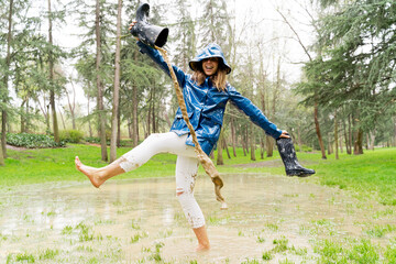 Side view of woman walking barefoot on pond empty galoshes with stream of water. Horizontal panoramic view of woman splashing with mud on rainy pond. Nature and people backgrounds.