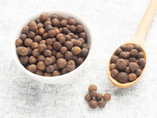 Spice Allspice (Jamaica pepper, Pimento) in white ceramic bowl wooden spoon and bunch on white concrete background. Macro. Indian cuisine concept
