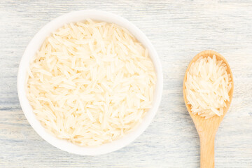 Long Basmati rice in ceramic bowl and wooden spoon on white wooden background. Macro. Flat lay. Healthy food concept