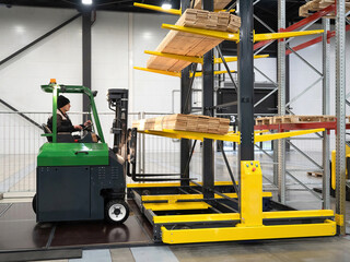 Forklift in stock. Warehouse worker operates forklift. Steel racks with boards. Man works at lumber...