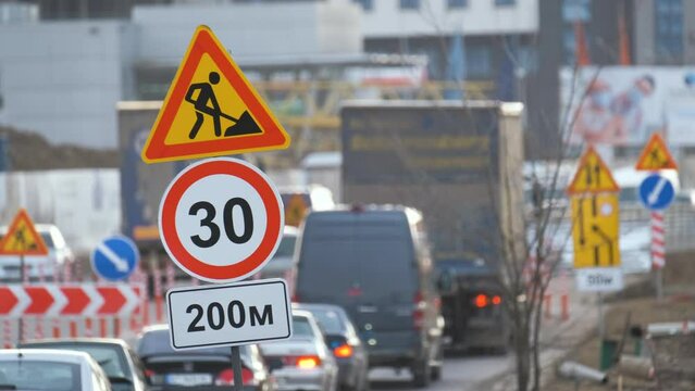 Roadworks warning traffic signs of construction work on city street and slowly moving cars