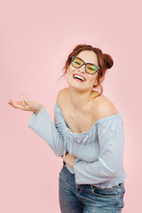 Chatty eccentric lady laughing, talking and gesturing. Her hair in buns. She has glasses in a thick black frame. Over pink background.