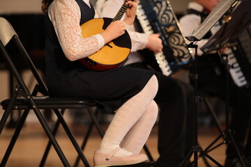 A student girl plays the balalaika in an ensemble of musicians in a lesson at school