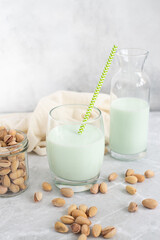 pistachio milk in a glass and in a bottle with straw and pistachios on a grey background. Vertical frame.
