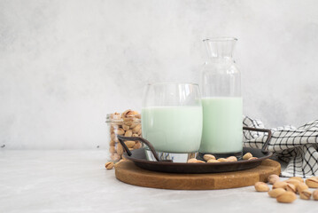 pistachio milk in a glass and in a bottle with pistachios on a plate grey background.