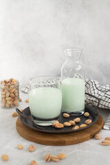 pistachio milk in a glass and in a bottle with pistachios on a plate grey background. vertical frame.