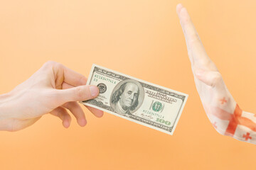 Say no dollar. The hand gesture of Georgia rejects dollars. One arm holds 100 dollars, and the other arm painted with the Georgian flag doesn't want to take it. Isolated on yellow background. Refuse