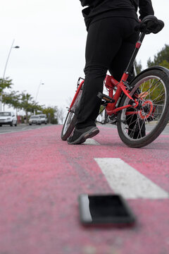 Vertical image, low angle, a girl in sportswear stops her bike in the bike lane to pick up her dropped cell phone.
