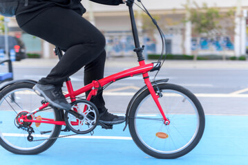 Side view of a real girl pedaling a red bike on a blue bike path in a city.