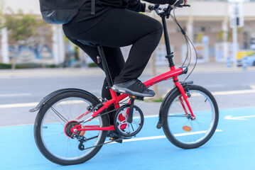 Side view of real legs pedaling at high speed in a city, the bicycle is red and is riding in a blue bike lane.