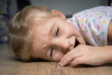 Frightened screaming child girl in t-shirt lying on wooden floor.